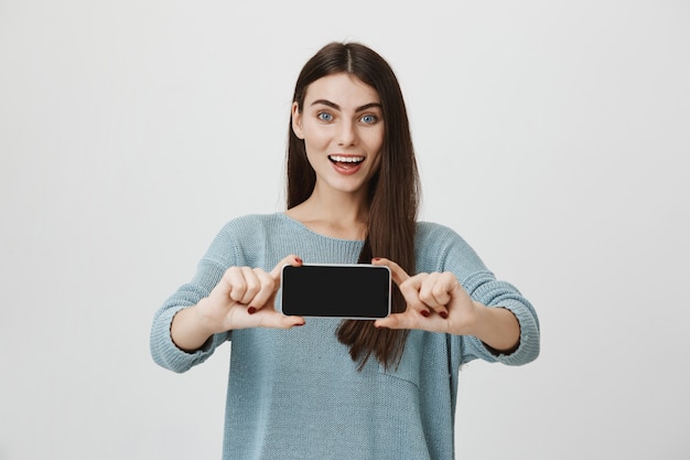 Mujer emocionada sorprendida que muestra la pantalla del teléfono inteligente