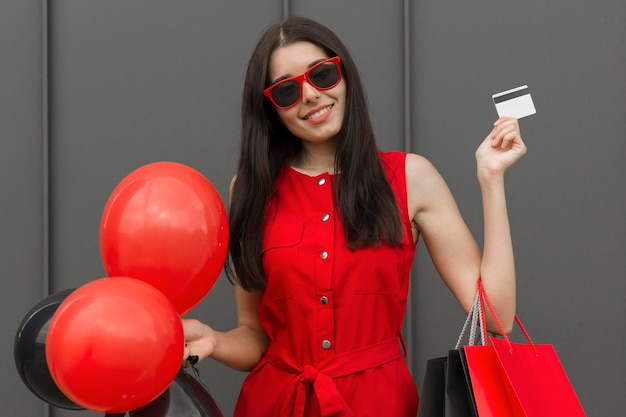 Mujer emocionada sosteniendo globos y tarjeta comercial plano medio