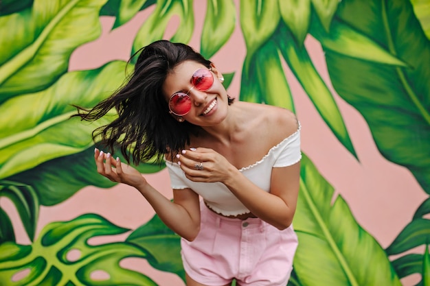 Foto gratuita mujer emocionada con tatuaje riendo frente a graffiti chica atractiva expresando felicidad en el día de verano