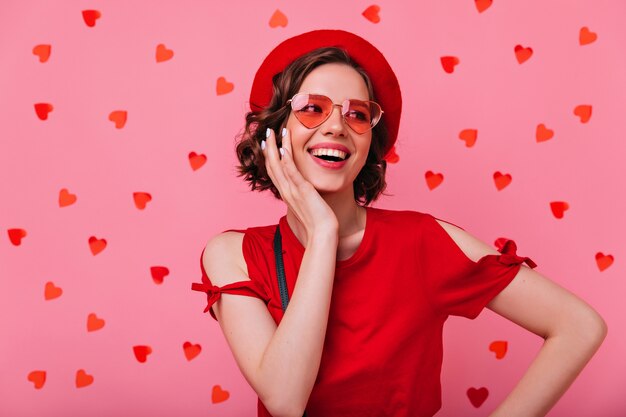 Mujer emocional alegre posando bajo confeti rojo. Feliz chica francesa divirtiéndose