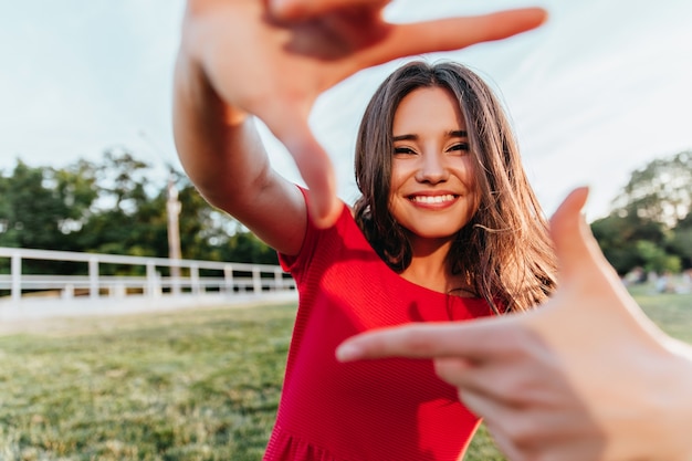 Mujer emocional alegre posando en el parque. chica con cabello oscuro brillante divirtiéndose al aire libre.