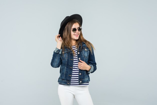 La mujer emocional joven en un sombrero negro está bailando en el fondo blanco