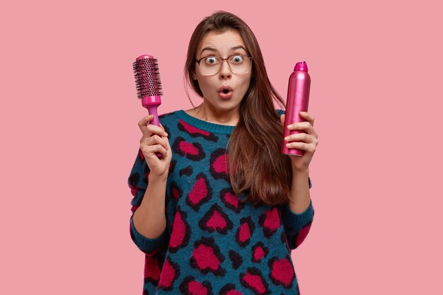 Mujer emotiva estupefacta emocional en el salón de belleza, sorprendida por el nuevo peinado, mira con los ojos muy abiertos, vestida con un suéter con manchas rosadas