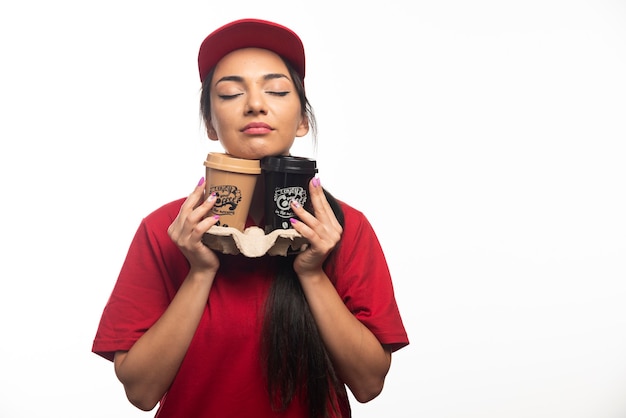 Mujer empleada de entrega en gorra roja abrazando dos tazas de café