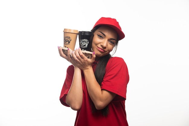 Mujer empleada de entrega en gorra roja abrazando dos tazas de café