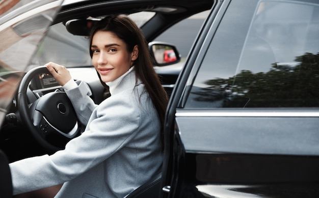 Mujer empresaria elegante se sube al coche para conducir el trabajo Mujer de negocios sonriente abre la puerta del vehículo y mira la cámara