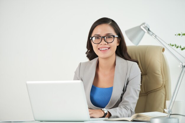 Mujer empresaria sonriendo con confianza a la cámara sentada en el escritorio