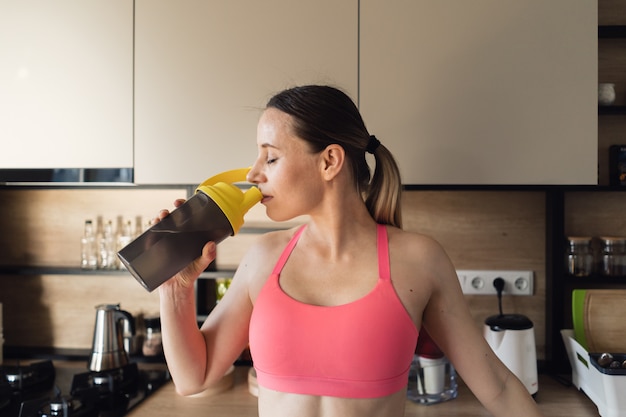 Mujer encantada beber agua después de hacer ejercicio en casa