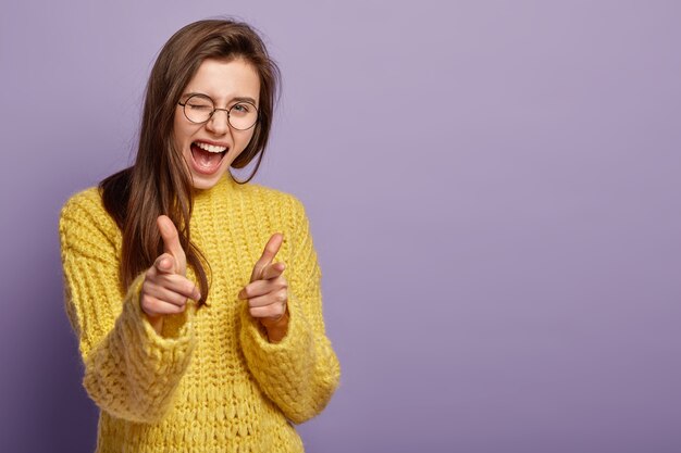 Mujer encantadora y alegre parpadea, exclama de felicidad, te señala, demuestra su elección