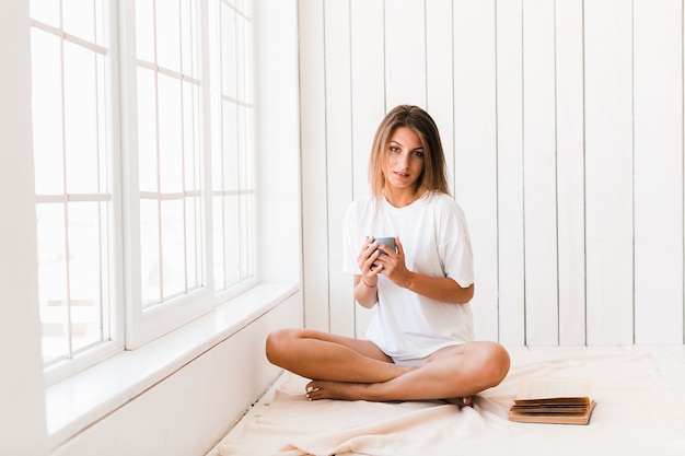 Mujer encantadora con bebida sentada junto a la ventana