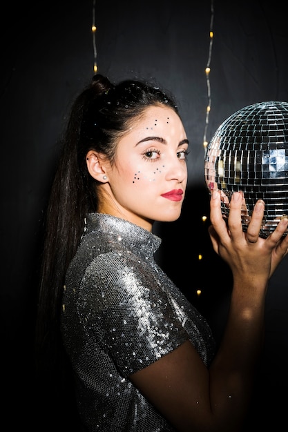 Foto gratuita mujer encantadora con brillos en cara sosteniendo bola de discoteca