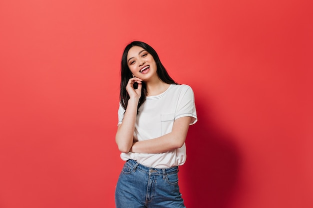 Mujer encantadora en camiseta ligera sonriendo lindo en pared roja