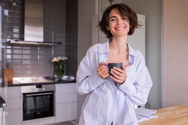 Mujer encantadora en casa sonriendo y sosteniendo una taza