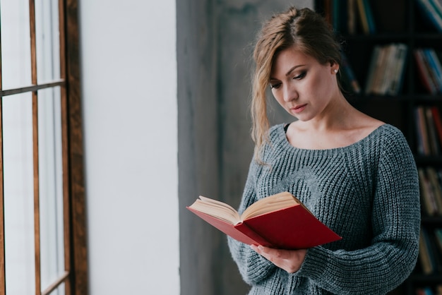 Mujer encantadora disfrutando leyendo cerca de la ventana