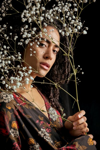 Mujer encantadora étnica atractiva con ramitas de flores en la oscuridad