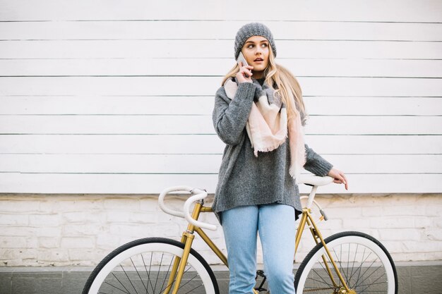 Mujer encantadora hablando por teléfono cerca de bicicleta