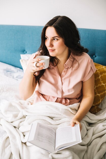 Mujer encantadora leyendo y bebiendo en la cama