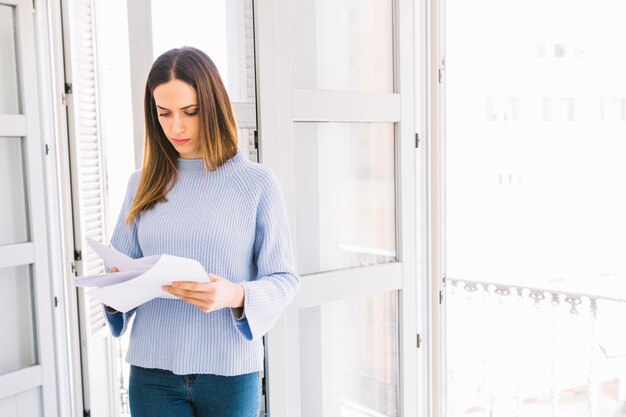 Mujer encantadora leyendo papeles junto a la ventana