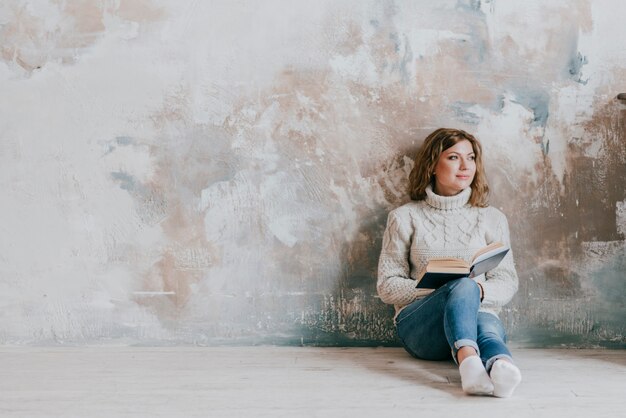 Mujer encantadora con libro cerca de la pared