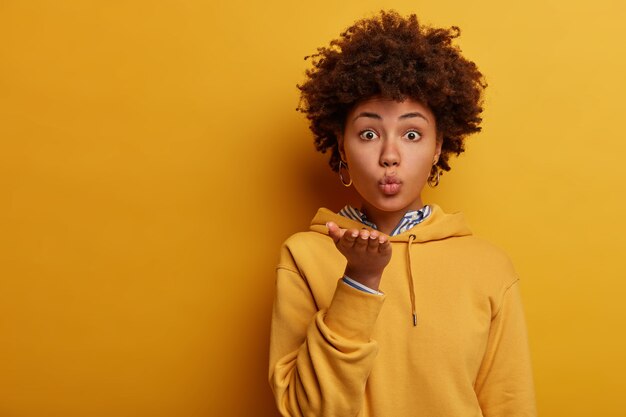 Mujer encantadora mantiene los labios doblados, envía beso al aire