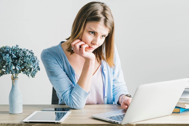 Mujer encantadora que piensa y que usa la computadora portátil