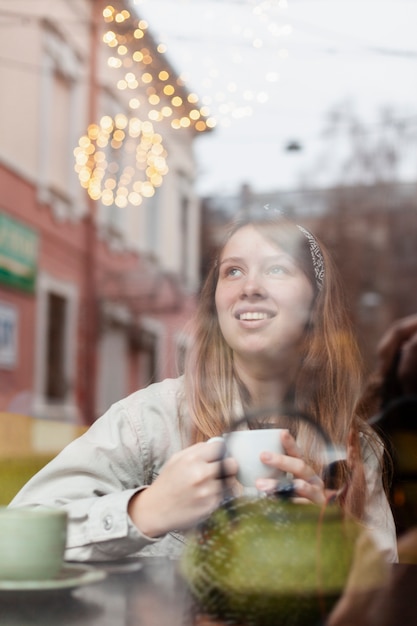 Foto gratuita mujer encantadora que sostiene el café a través de la ventana