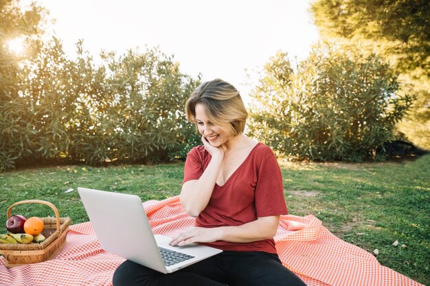 Mujer encantadora que usa la computadora portátil en comida campestre