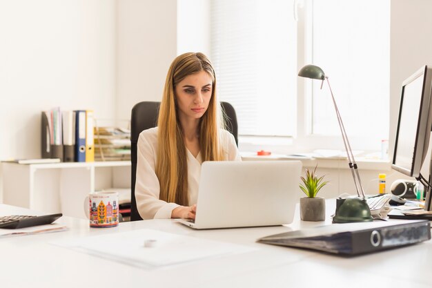 Mujer encantadora que usa la computadora portátil en oficina