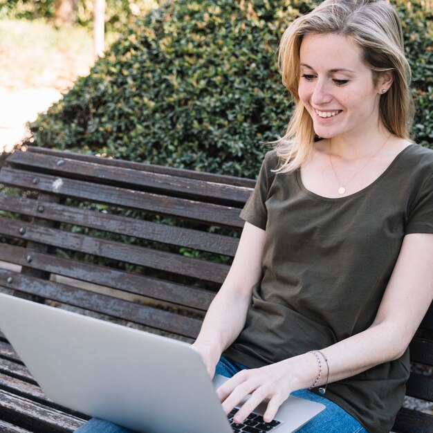 Mujer encantadora que usa la computadora portátil en el parque