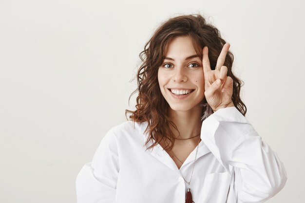 Mujer encantadora sonriente mostrando un signo de la paz cerca de su rostro