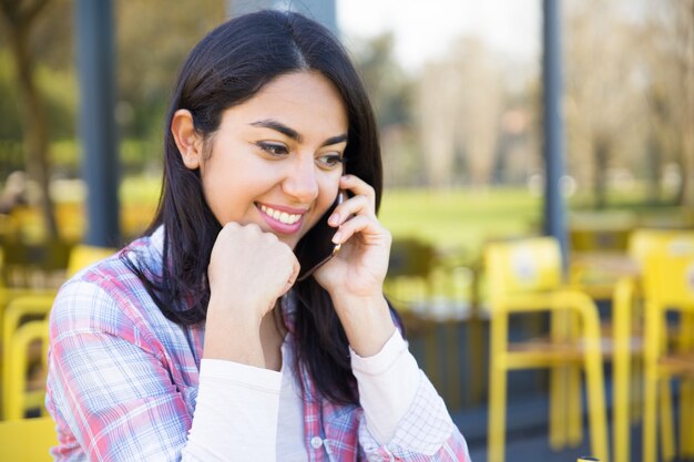 Mujer encantadora sonriente que habla en el teléfono móvil en café de la calle