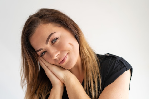 Mujer encantadora sonriente que lleva a cabo las manos juntas y que toca la cara