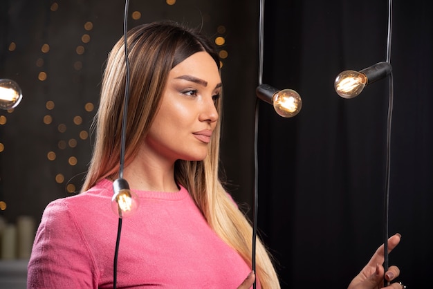 Una mujer encantadora en suéter posando junto a lámparas de luz.