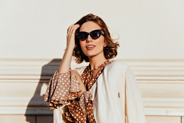 Mujer encantadora en traje vintage expresando interés. Tiro al aire libre de glamorosa niña feliz en gafas de sol.