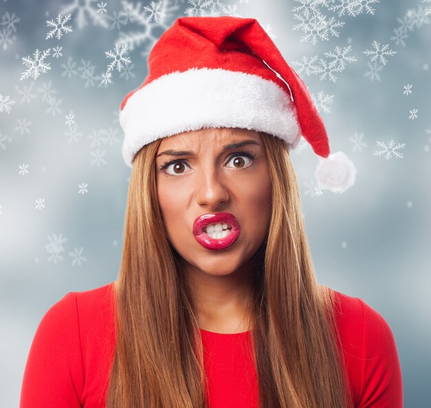 Mujer enfadada con el sombrero de papa noel en un fondo de copos de nieve