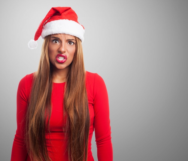 Mujer enfadada con el sombrero de papa noel en fondo gris