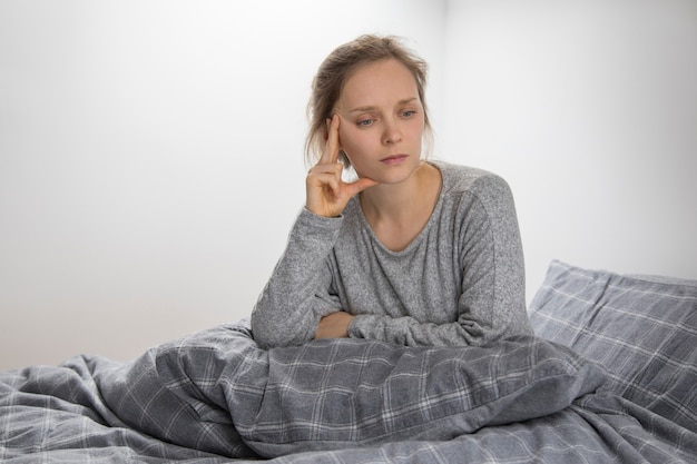 Mujer enferma en la cama con la almohada en las rodillas, mirando a un lado