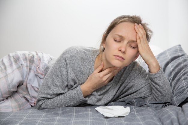 Mujer enferma cansada en la cama con los ojos cerrados que tiene dolor de garganta