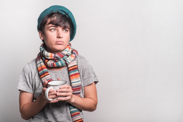 Foto gratuita mujer enferma contemplada que sostiene la taza de café contra fondo gris