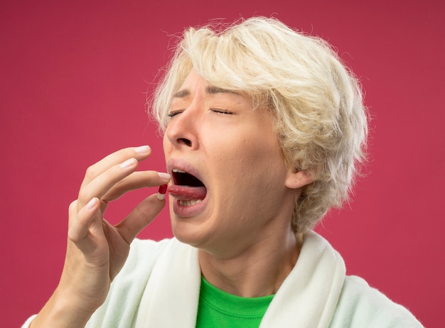 Foto gratuita mujer enferma enferma con el pelo corto que se siente mal tomando la píldora con expresión de disgusto de pie sobre la pared rosa