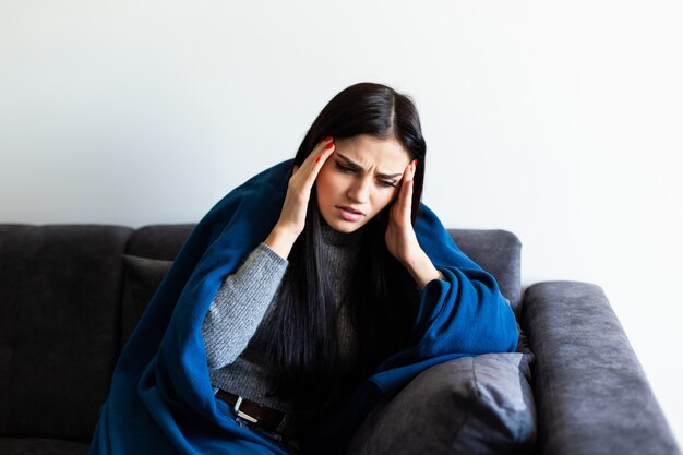Mujer enferma indispuesta que siente su temperatura mientras descansa en el sofá de casa