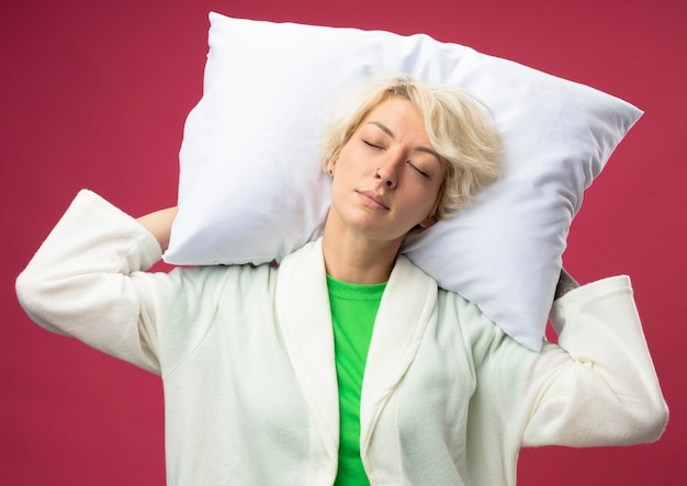 Foto gratuita mujer enferma malsana con pelo corto sosteniendo la almohada con los ojos cerrados de pie sobre fondo rosa