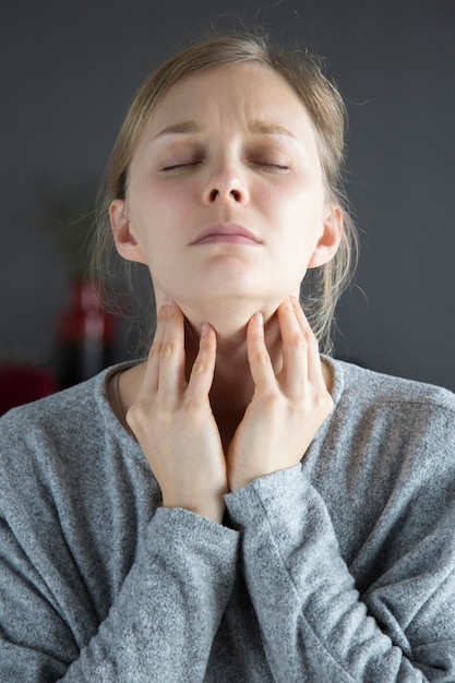 Mujer enferma con los ojos cerrados que tiene dolor de garganta, tocar el cuello