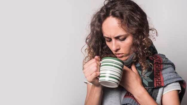 Mujer enferma que mira en la taza de café contra el fondo blanco