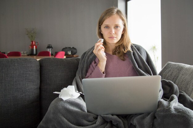 Mujer enferma que trabaja en la computadora portátil en el sofá en casa
