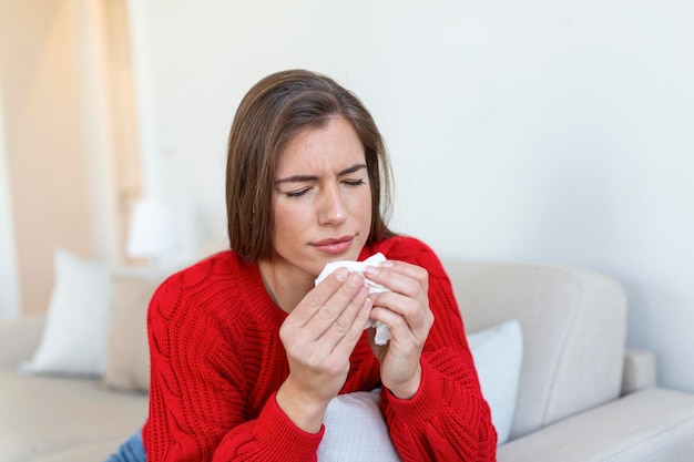 Una mujer enferma sentada en la cama se siente poco saludable sonarse la nariz, una mujer joven enferma que sufre de rinitis, tiene una infección respiratoria, necesita medicación