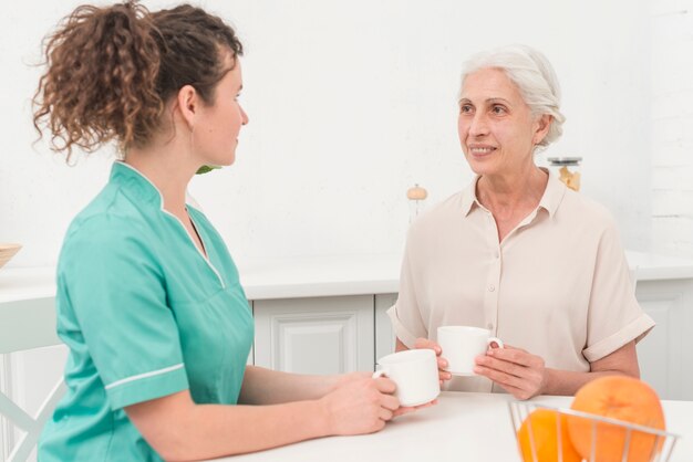 Mujer enfermera tomando café con mujer senior