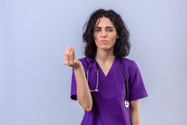 Mujer enfermera en uniforme médico y con estetoscopio haciendo gesto de dinero con las manos pidiendo pago de salario de pie en blanco aislado