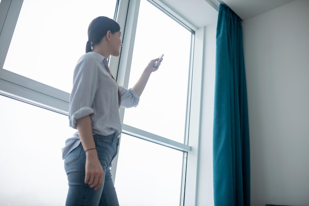 Mujer enfocada usando un gadget para abrir las cortinas