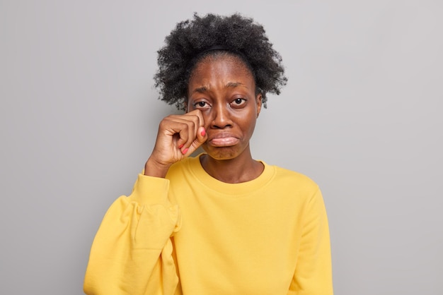 mujer enjuga lágrimas debajo del ojo se siente deprimido y deprimido los labios usa junmper amarillo casual aislado en gris se arrepiente de algo se queja en la vida desafortunada